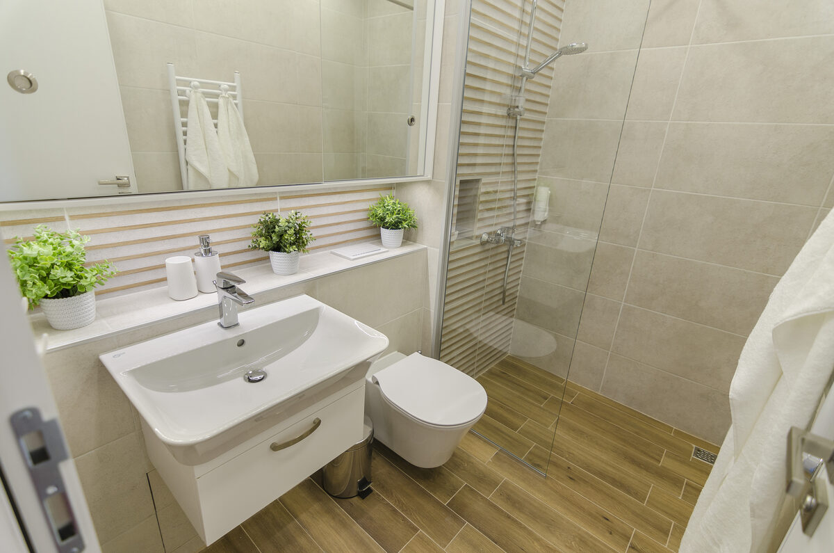 Modern bathroom with walk-in glass shower, wood-tone flooring, and beige tiles