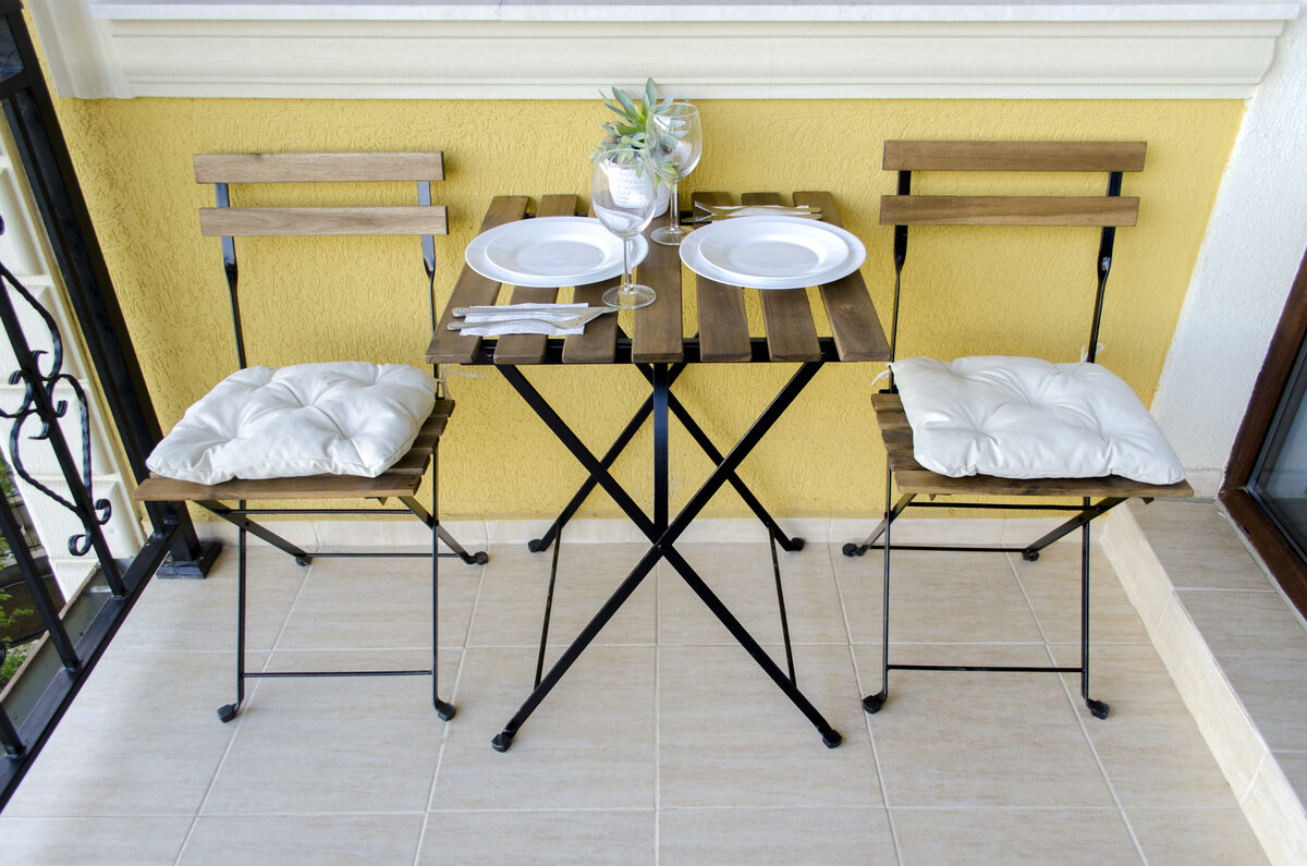 Intimate balcony bistro set with two chairs and small table against yellow wall