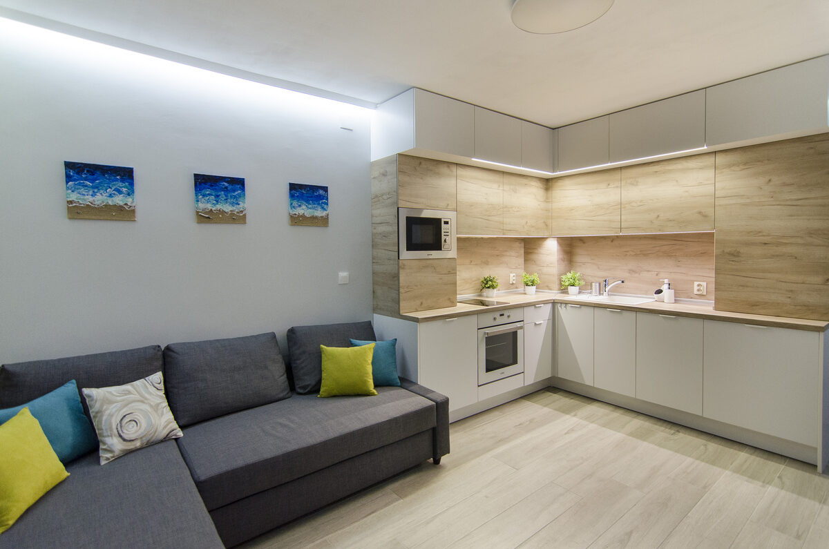 Living area with L-shaped gray sofa, ocean-themed wall art, and open kitchen